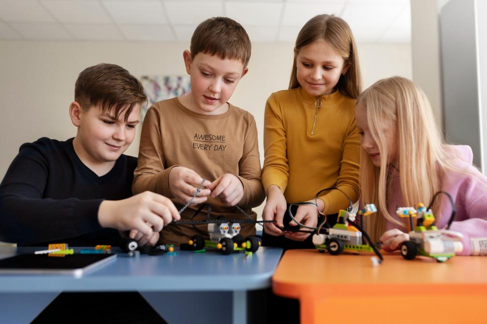 Czworo dzieci siedzi przy stoliku i wspólnie buduje modele robotów z klocków oraz przewodów.