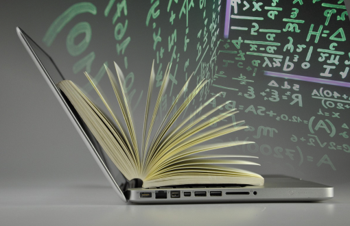 Otwarty laptop, na nim otwarta książka. Nad nią widoczne kolorowe wzory matematyczne. 